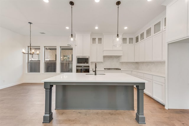 kitchen featuring tasteful backsplash, light countertops, appliances with stainless steel finishes, a sink, and an island with sink