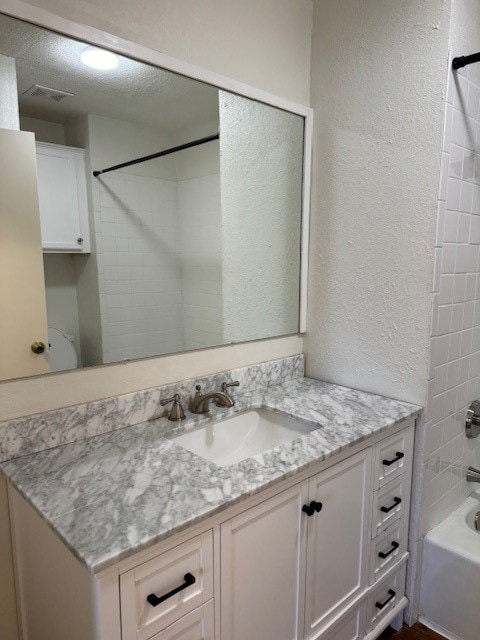 bathroom with tiled shower / bath, vanity, and a textured ceiling