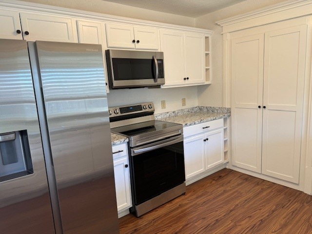 kitchen with white cabinets, light stone counters, stainless steel appliances, and dark hardwood / wood-style flooring