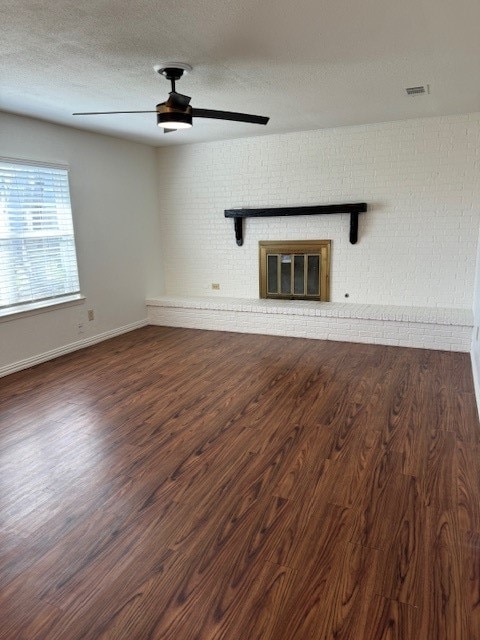 unfurnished living room featuring ceiling fan, a textured ceiling, a brick fireplace, and dark hardwood / wood-style floors