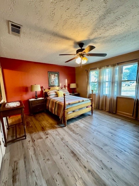 bedroom with hardwood / wood-style floors, multiple windows, a textured ceiling, and ceiling fan