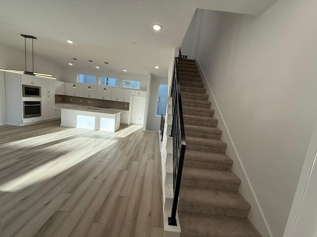 interior space featuring white cabinetry, decorative light fixtures, appliances with stainless steel finishes, a kitchen island, and light hardwood / wood-style floors