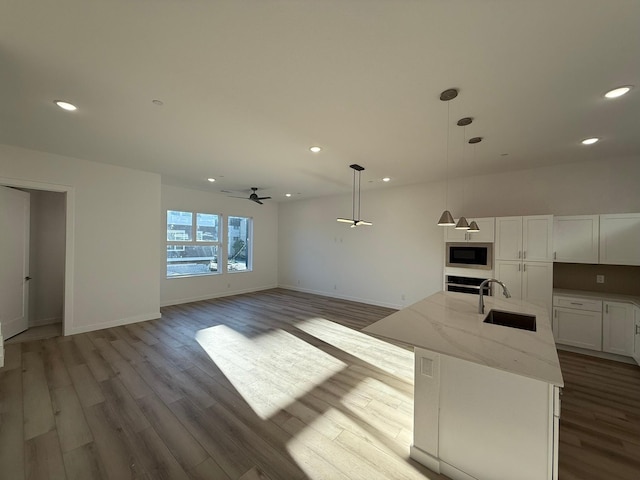 kitchen featuring light stone counters, an island with sink, white cabinets, built in microwave, and decorative light fixtures