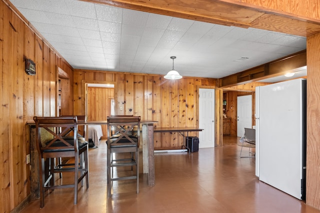 kitchen with wood walls, decorative light fixtures, white refrigerator, and a breakfast bar area