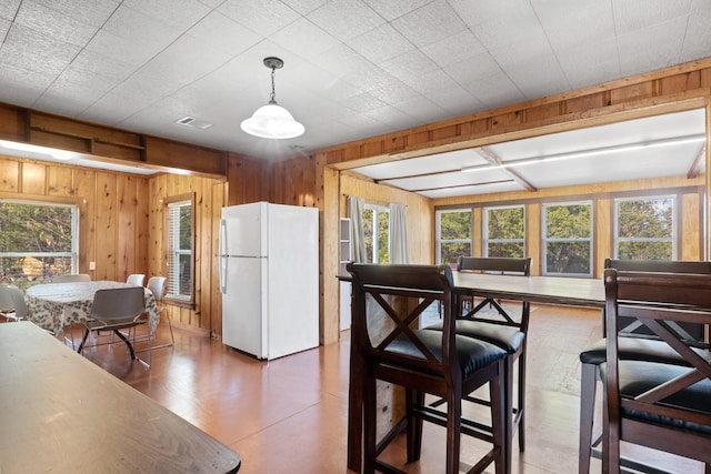 kitchen with visible vents, hanging light fixtures, freestanding refrigerator, and wooden walls