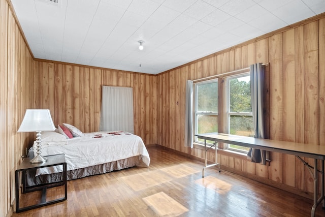 bedroom with crown molding, wood-type flooring, and wooden walls