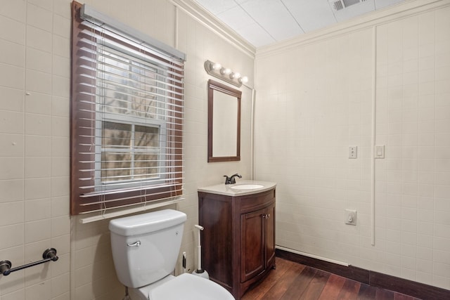 half bath featuring wood finished floors, visible vents, vanity, tile walls, and ornamental molding