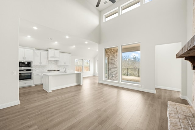 unfurnished living room with light wood-type flooring, ceiling fan, sink, and a high ceiling