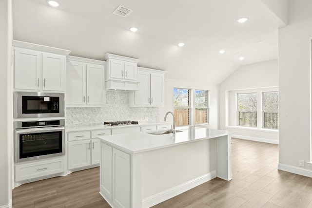 kitchen with vaulted ceiling, appliances with stainless steel finishes, white cabinetry, an island with sink, and sink