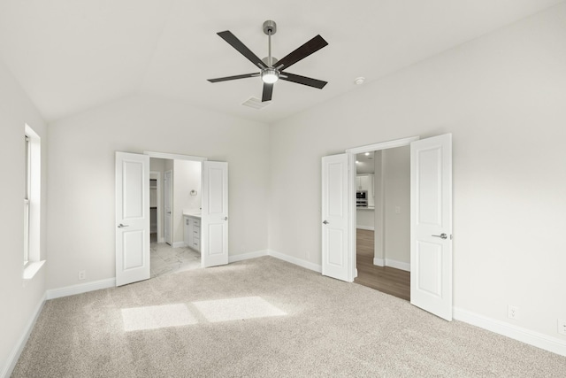 unfurnished bedroom with ceiling fan, ensuite bathroom, light carpet, and lofted ceiling