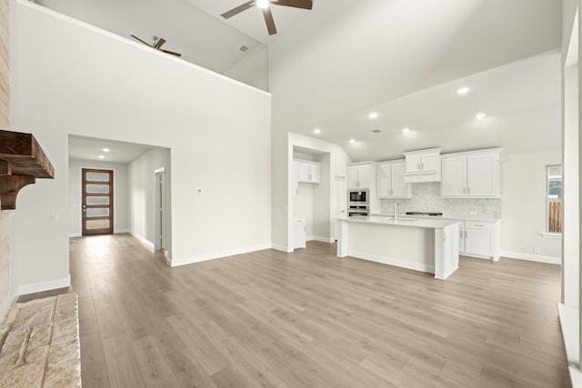 unfurnished living room featuring ceiling fan, sink, high vaulted ceiling, and light hardwood / wood-style floors