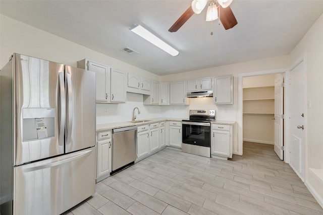 kitchen with stainless steel appliances, sink, white cabinetry, light stone counters, and ceiling fan