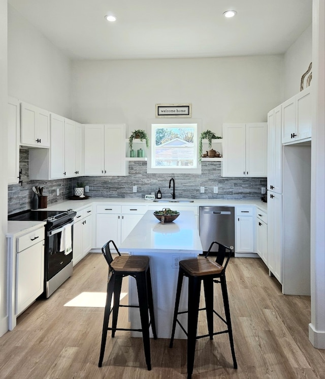 kitchen with light hardwood / wood-style floors, sink, a breakfast bar area, stainless steel appliances, and white cabinets