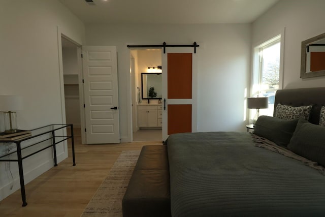 bedroom with ensuite bathroom, light hardwood / wood-style flooring, and a barn door