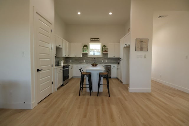 kitchen featuring light hardwood / wood-style floors, a kitchen island, white cabinetry, appliances with stainless steel finishes, and a breakfast bar area