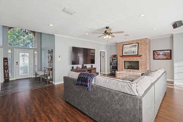 living room with dark wood-type flooring, crown molding, a fireplace, and ceiling fan