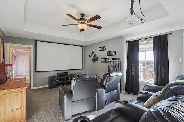 carpeted cinema with ceiling fan and a tray ceiling