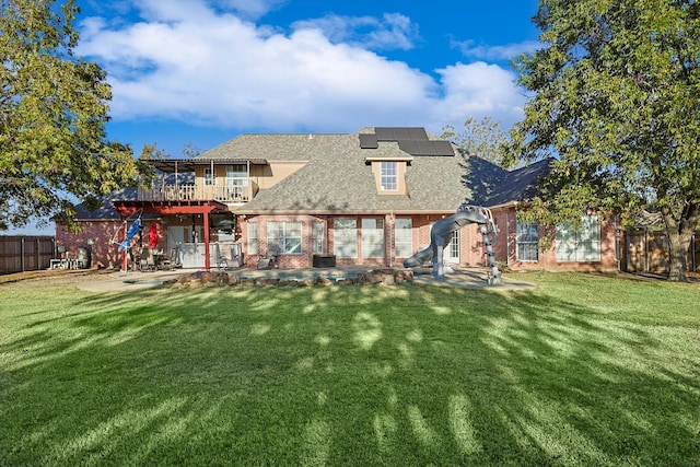 back of house with a balcony, a yard, a patio area, and solar panels