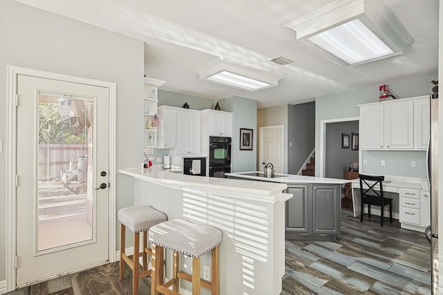 kitchen featuring kitchen peninsula, white cabinets, dark hardwood / wood-style flooring, a breakfast bar, and black double oven