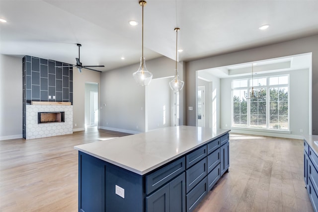 kitchen with blue cabinets, light hardwood / wood-style flooring, a kitchen island, pendant lighting, and a fireplace