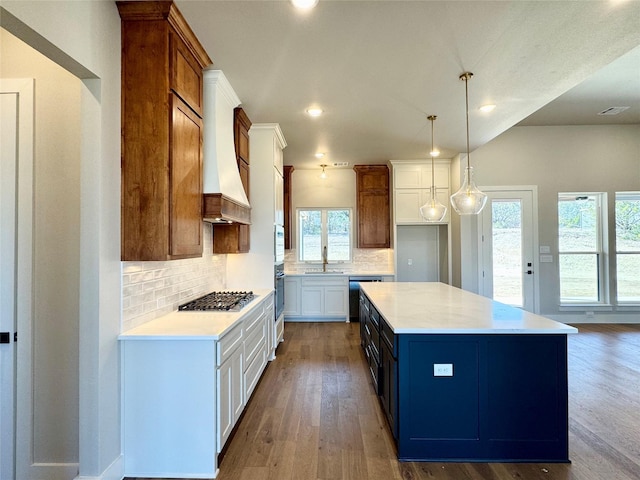 kitchen with decorative light fixtures, stainless steel gas stovetop, white cabinetry, sink, and a center island