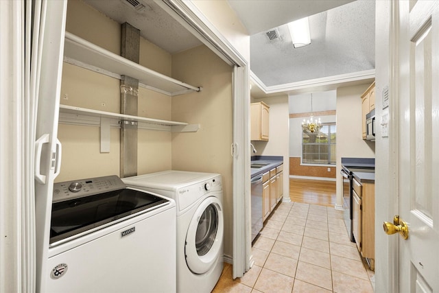 washroom featuring a textured ceiling, sink, light tile patterned floors, an inviting chandelier, and washing machine and dryer