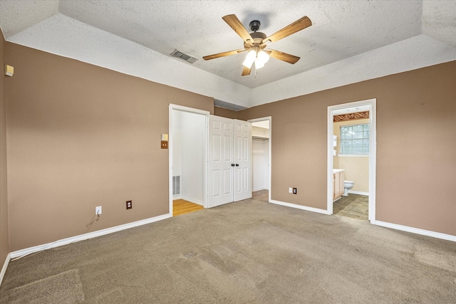 unfurnished bedroom with a raised ceiling, ensuite bathroom, and ceiling fan