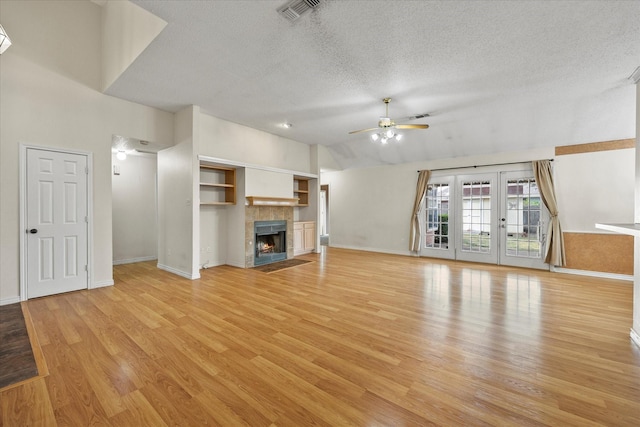 unfurnished living room with french doors, light hardwood / wood-style floors, ceiling fan, and a tiled fireplace