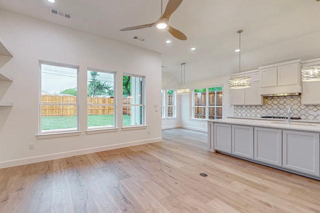 kitchen featuring decorative backsplash, hanging light fixtures, ceiling fan, light hardwood / wood-style flooring, and sink