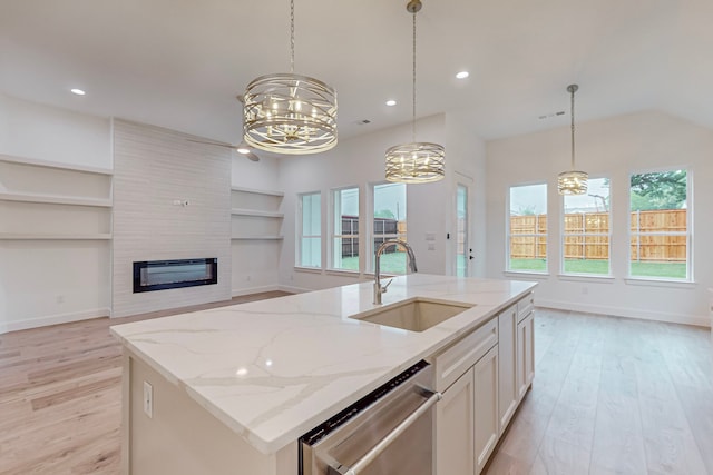 kitchen with a kitchen island with sink, sink, white cabinets, light stone counters, and light hardwood / wood-style floors