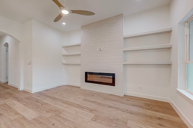 unfurnished living room featuring built in features, a fireplace, light wood-type flooring, and ceiling fan