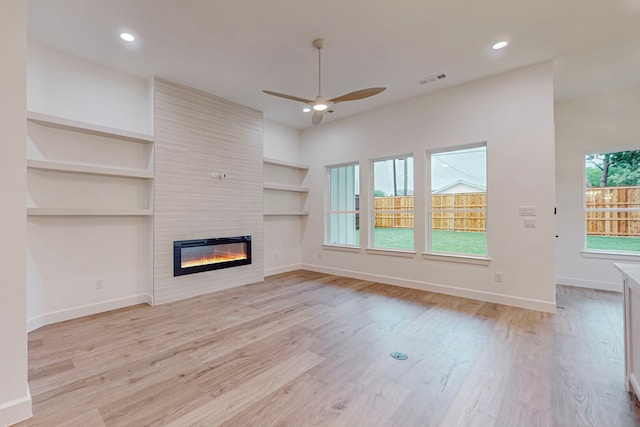 unfurnished living room with ceiling fan, a wealth of natural light, light wood-type flooring, and a fireplace