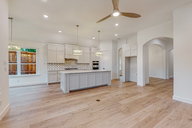 kitchen featuring decorative backsplash, hanging light fixtures, ceiling fan, a kitchen island with sink, and light hardwood / wood-style floors