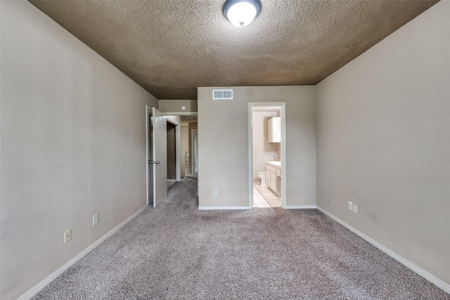 unfurnished bedroom featuring ensuite bath, light colored carpet, and a textured ceiling