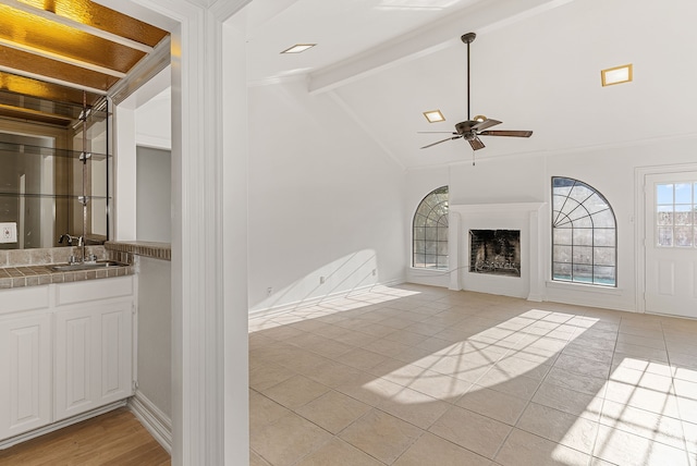 unfurnished living room featuring sink, lofted ceiling with beams, ceiling fan, and light tile patterned flooring