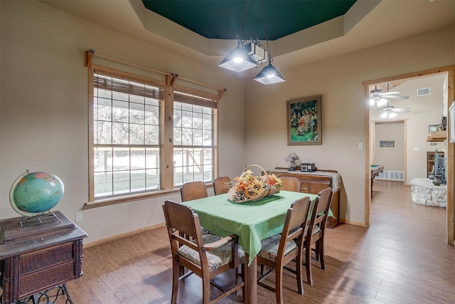 dining area with light hardwood / wood-style flooring, a raised ceiling, and ceiling fan