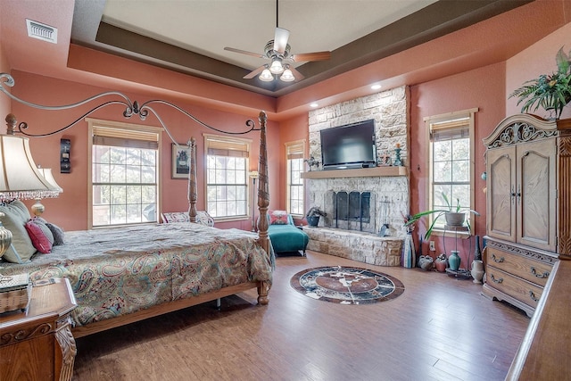 bedroom with a fireplace, hardwood / wood-style flooring, a raised ceiling, and ceiling fan