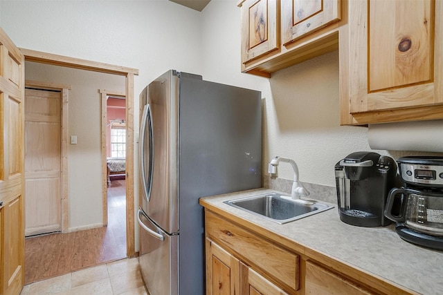 kitchen featuring stainless steel fridge, sink, light tile patterned floors, and light brown cabinets