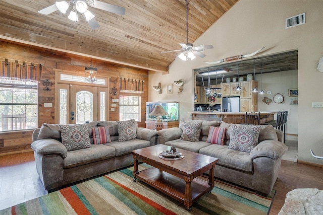 living room featuring ceiling fan with notable chandelier, hardwood / wood-style flooring, high vaulted ceiling, wooden ceiling, and wood walls