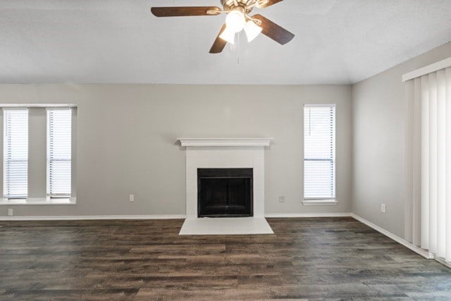 unfurnished living room featuring ceiling fan, a tiled fireplace, and dark hardwood / wood-style flooring