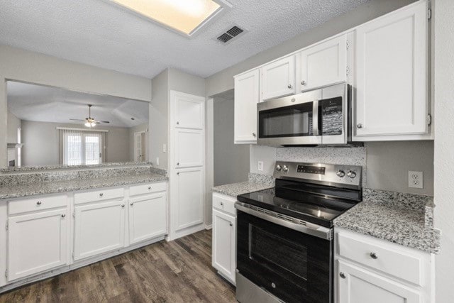 kitchen featuring dark wood-type flooring, white cabinets, appliances with stainless steel finishes, light stone counters, and a textured ceiling