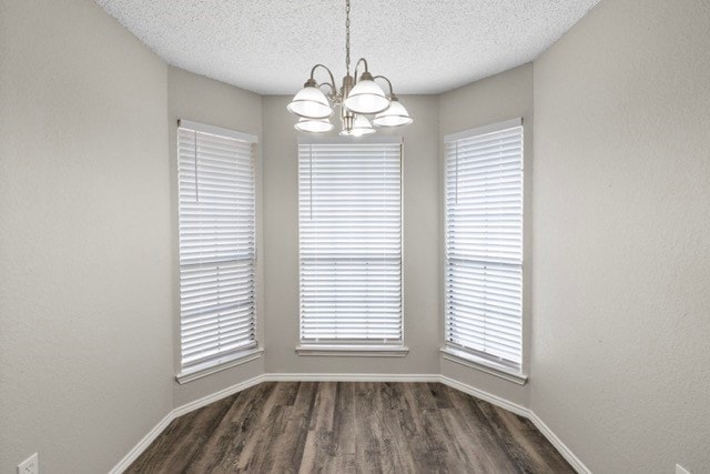 spare room featuring a textured ceiling, dark hardwood / wood-style floors, a chandelier, and a wealth of natural light