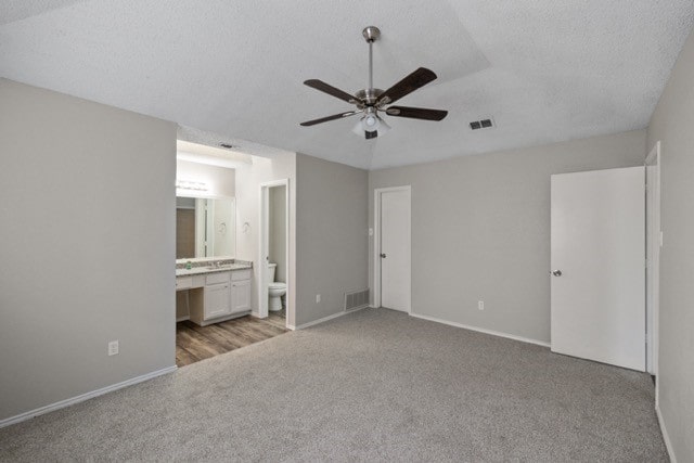 unfurnished bedroom with connected bathroom, a textured ceiling, light colored carpet, and ceiling fan