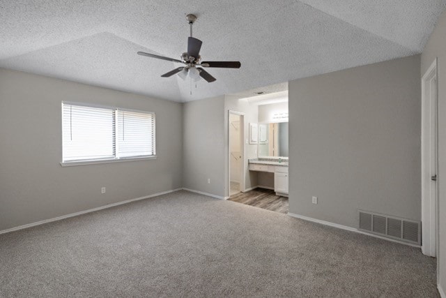 unfurnished bedroom featuring light carpet, lofted ceiling, ceiling fan, a textured ceiling, and connected bathroom