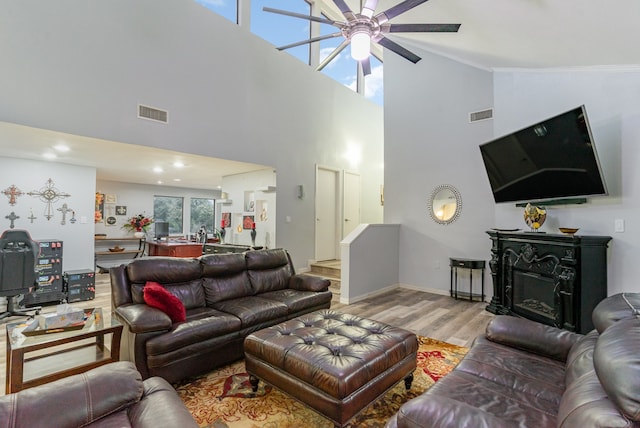 living room with ceiling fan, a towering ceiling, and light wood-type flooring