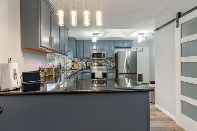 kitchen with hanging light fixtures, stainless steel appliances, a barn door, kitchen peninsula, and light wood-type flooring