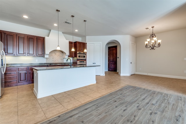 kitchen with decorative backsplash, a center island with sink, hanging light fixtures, a chandelier, and stainless steel appliances