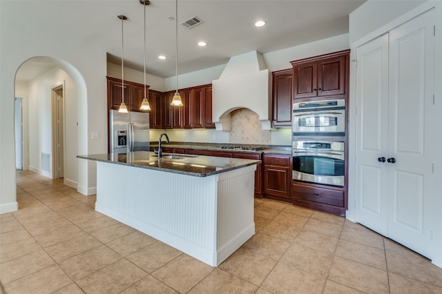 kitchen featuring tasteful backsplash, sink, an island with sink, hanging light fixtures, and stainless steel appliances