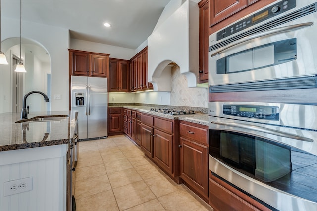 kitchen featuring appliances with stainless steel finishes, sink, decorative light fixtures, dark stone countertops, and light tile patterned floors