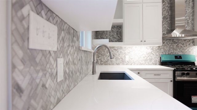 kitchen with wall chimney range hood, backsplash, stainless steel gas range, sink, and white cabinetry